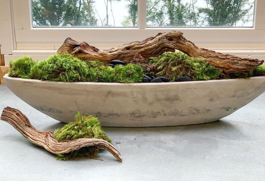 Wooden dough bowl filled with driftwood, moss, and rocks on countertop.