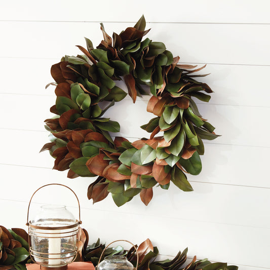 30" faux magnolia leaf wreath hanging on shiplap wall with candle hurricane.