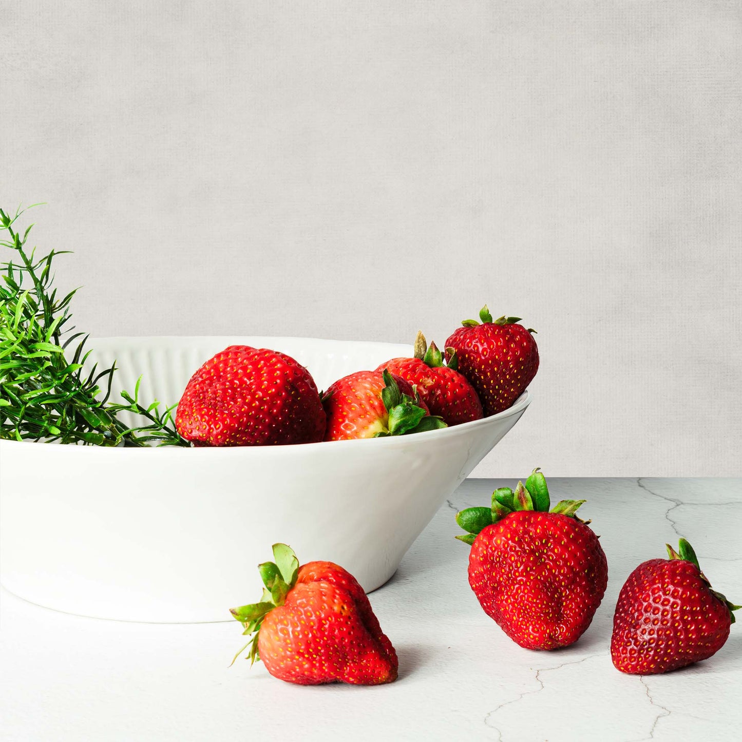 Artesa ceramic bowl filled with strawberries and rosemary on limestone table.