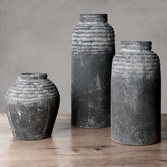 Artisanal gray earthenware vessel with weathered patina on wood floor with gray background.