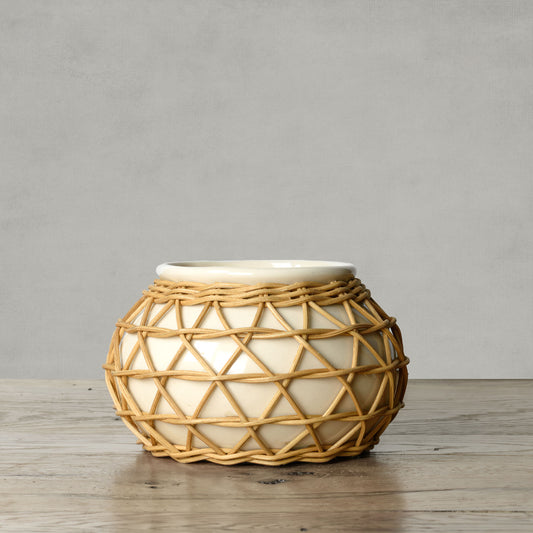 Artisanal natural rattan decorative ceramic planter on wood surface with gray background.