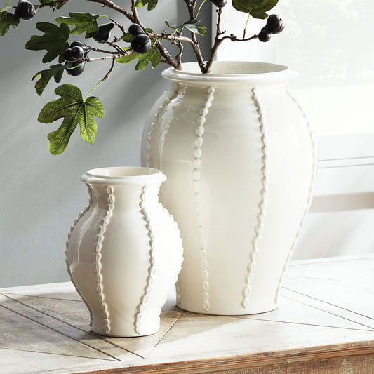 Beaded white ceramic vase stylized on table with jar and olive branches.