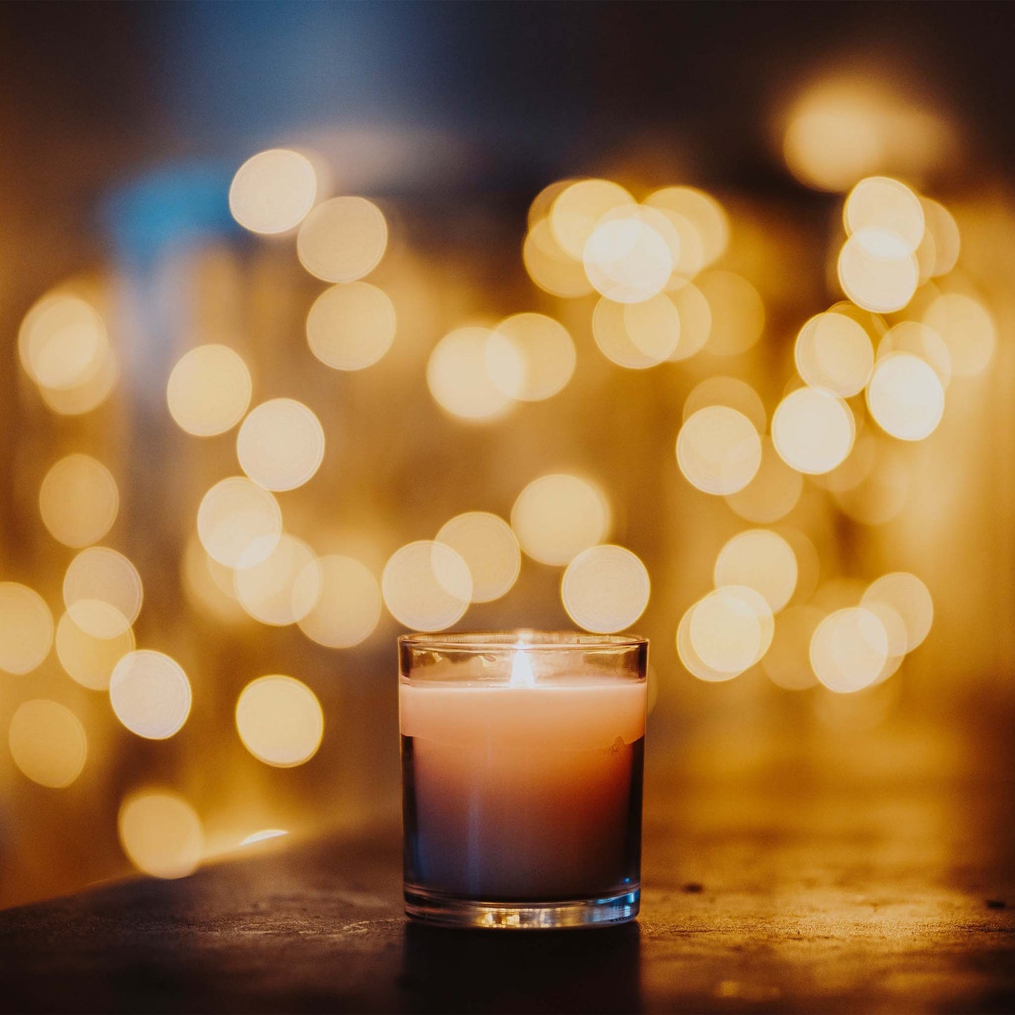 Luxury scented soy wax blend burning candle on farmhouse table with blurred backlighting.