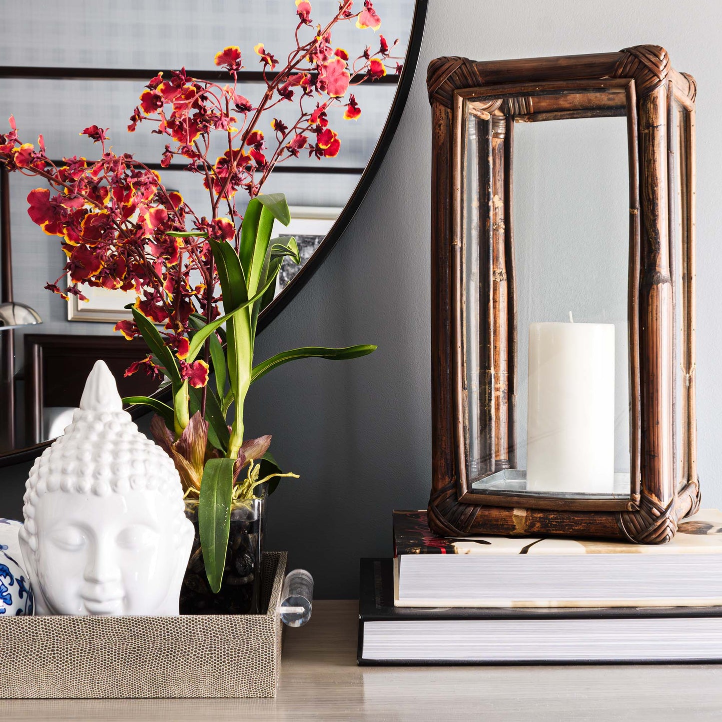 Cane rattan hurricane candleholder on stack of books, shagreen tray with buddha head and orchid.