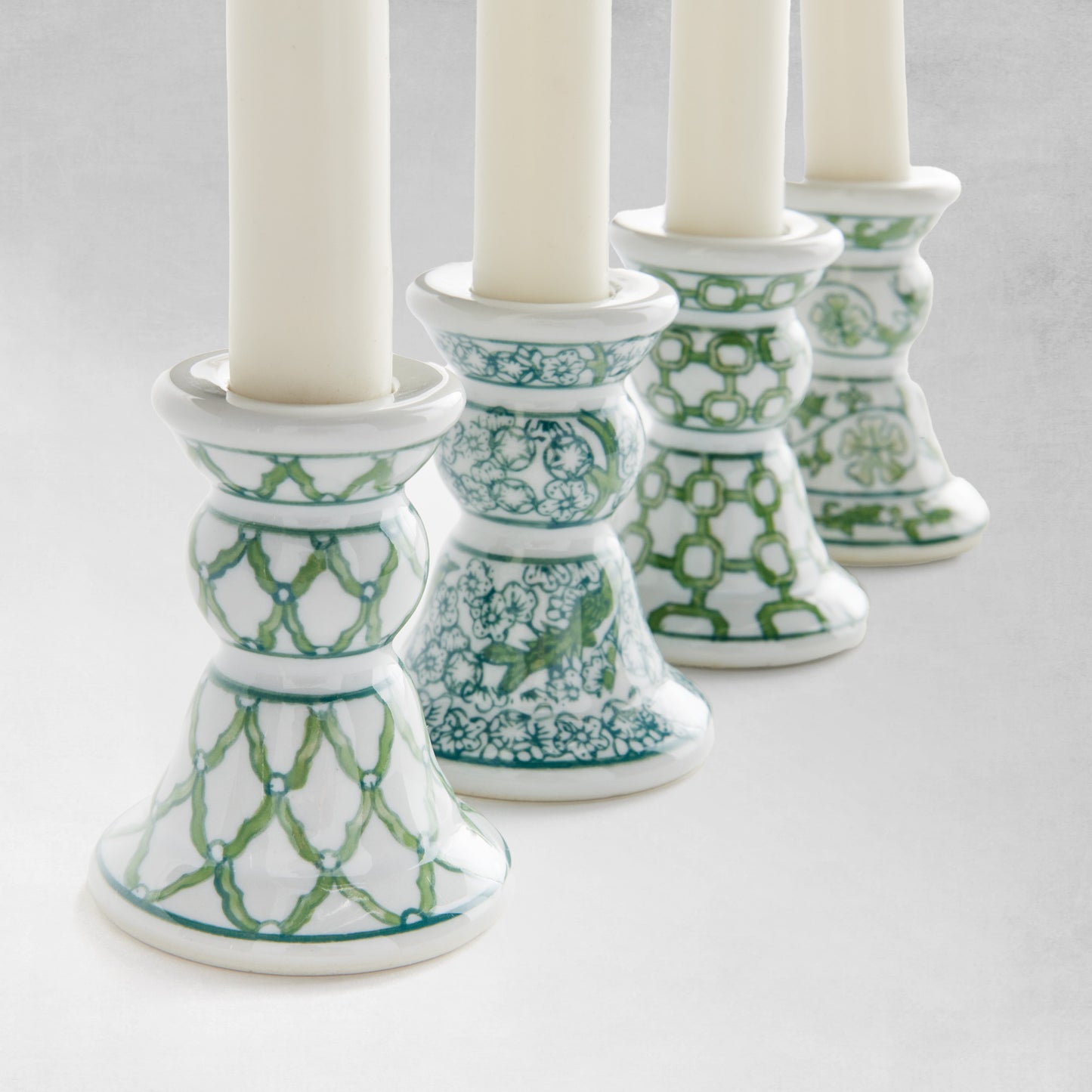 Chinoiserie green and white porcelain taper holders closeup view, with gray background.
