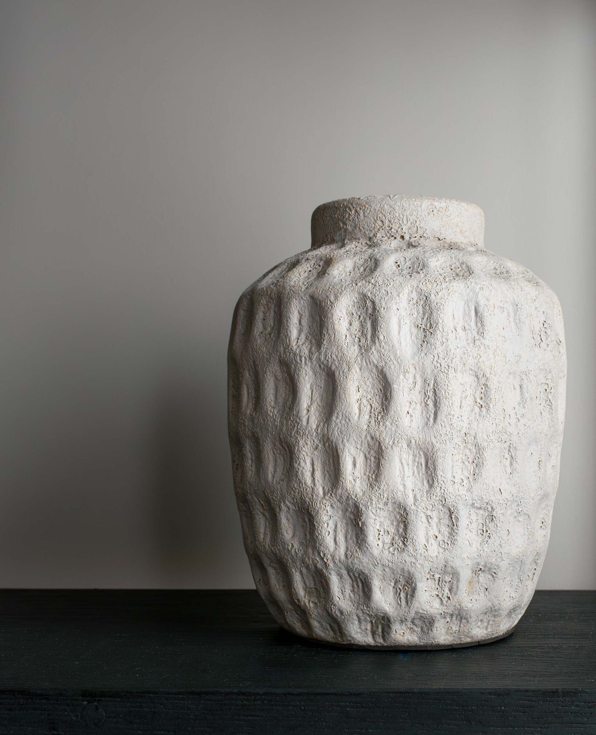 Concrete/cement decorative dimpled vase on black oak shelf.