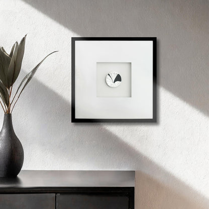 Contemporary framed art deco black and white colonial shell artwork on textured wall, plant in vase, black wooden console table.