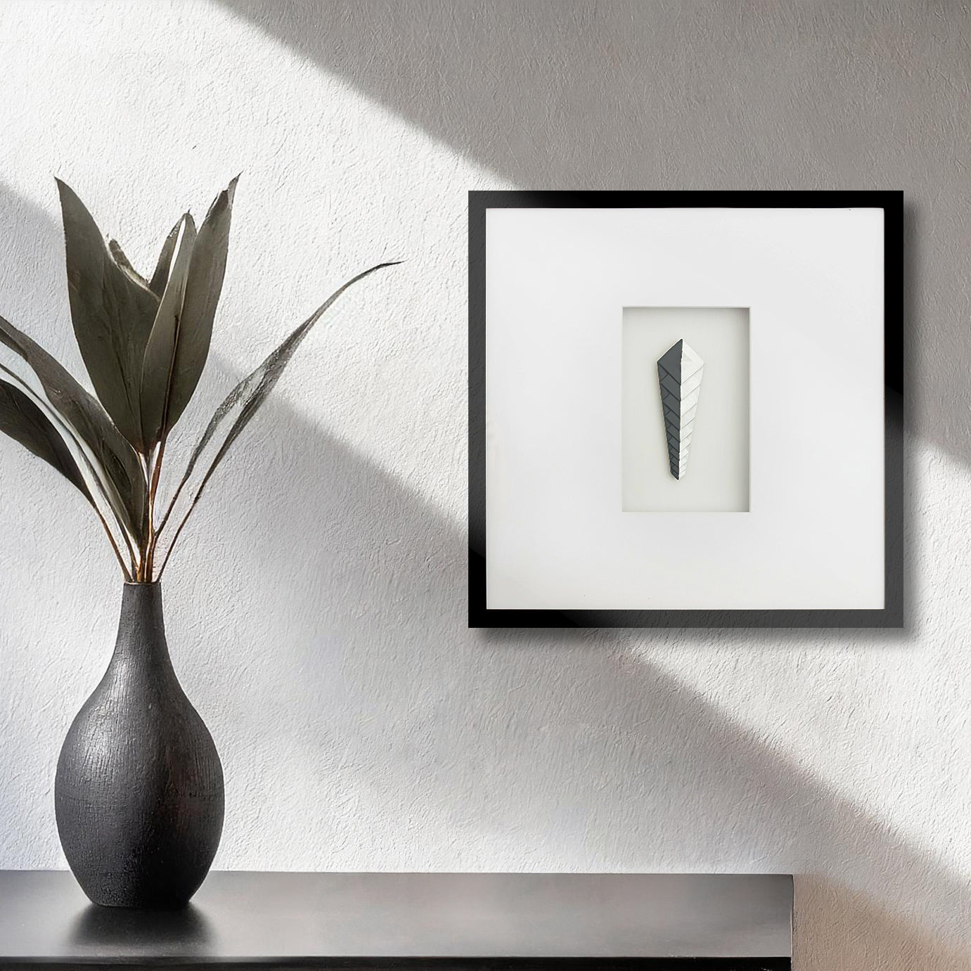 Contemporary framed art deco black and white artwork on textured wall with vase and plant.