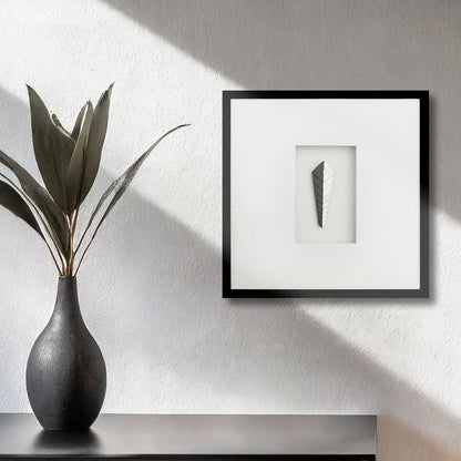 Contemporary framed art deco black and white artwork on textured wall with vase and plant.