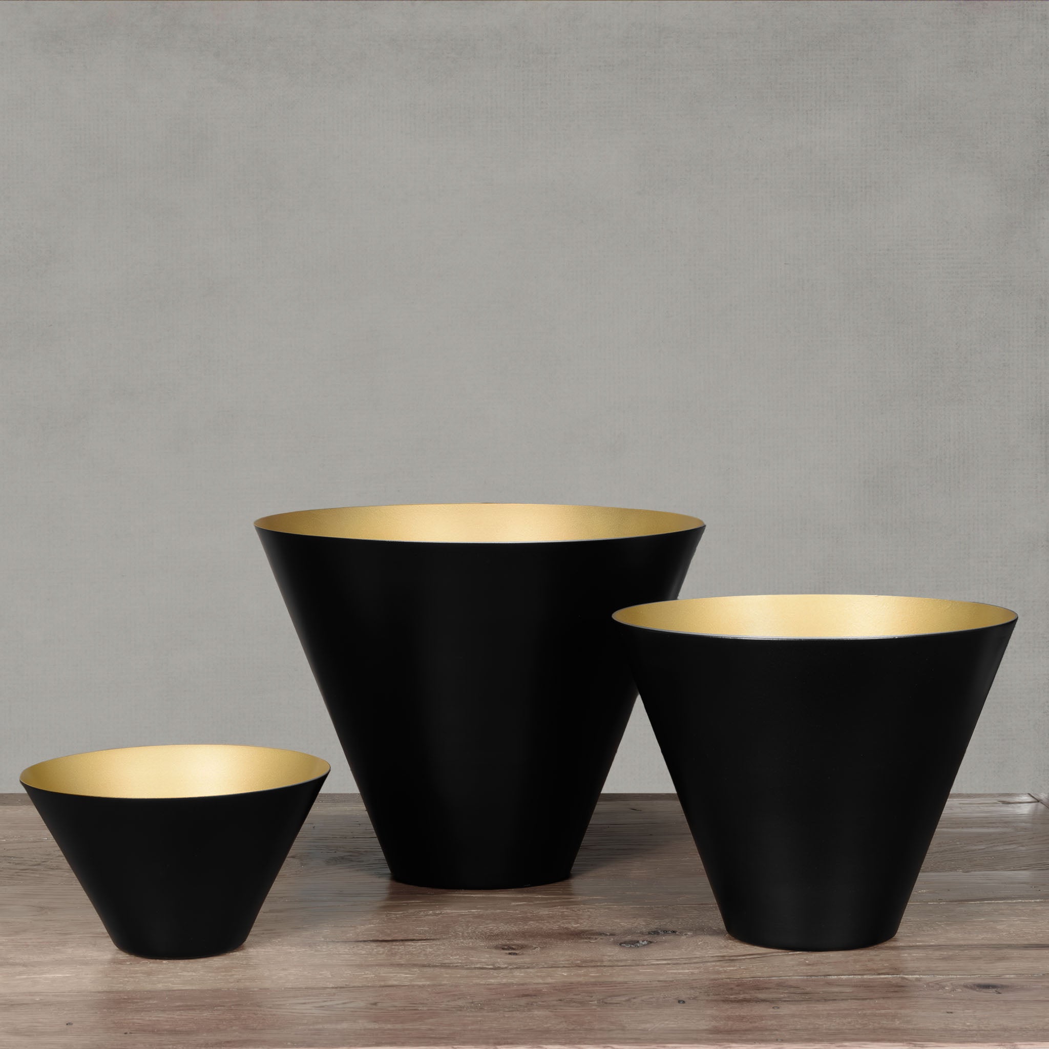 Decorative black and gold bowl set on wooden floor with gray background.