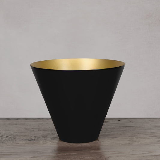 Decorative black and gold medium bowl on light gray wood floor with light gray background.