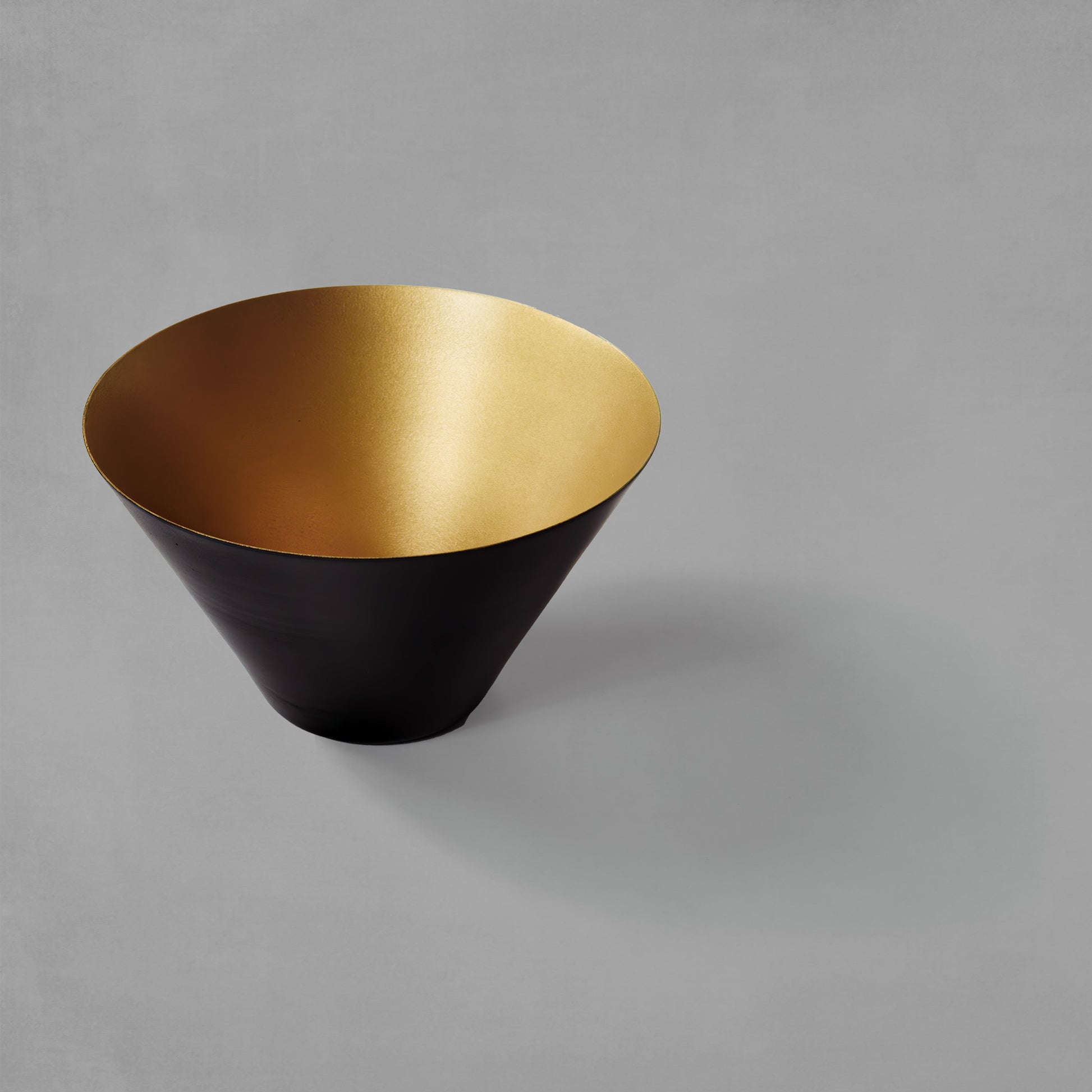 Small decorative black and gold bowl with gray background.
