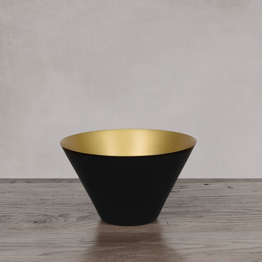 Decorative black and gold small bowl on light gray wood floor with light gray background.