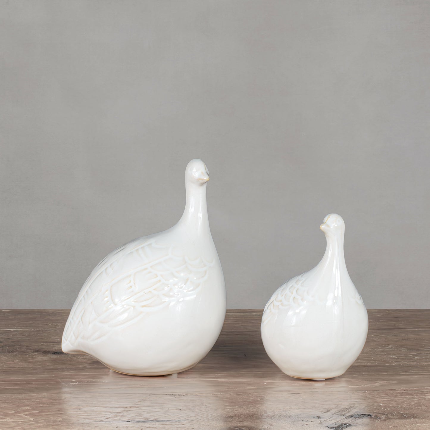 Decorative ceramic bird objects on wooden table with gray background.