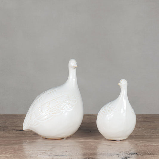 Decorative ceramic bird objects on wooden table with gray background.
