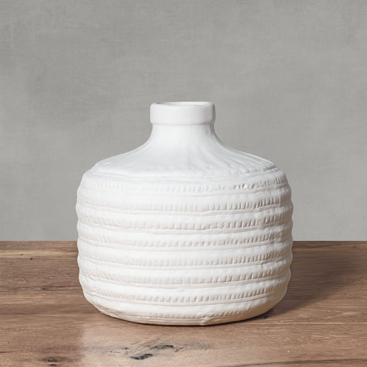 Decorative ceramic white vase with textured banding on wood surface with gray background.