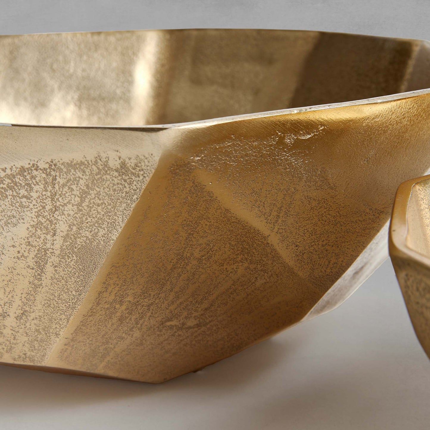 Decorative gold geometric bowls, closeup of side view, with gray background.