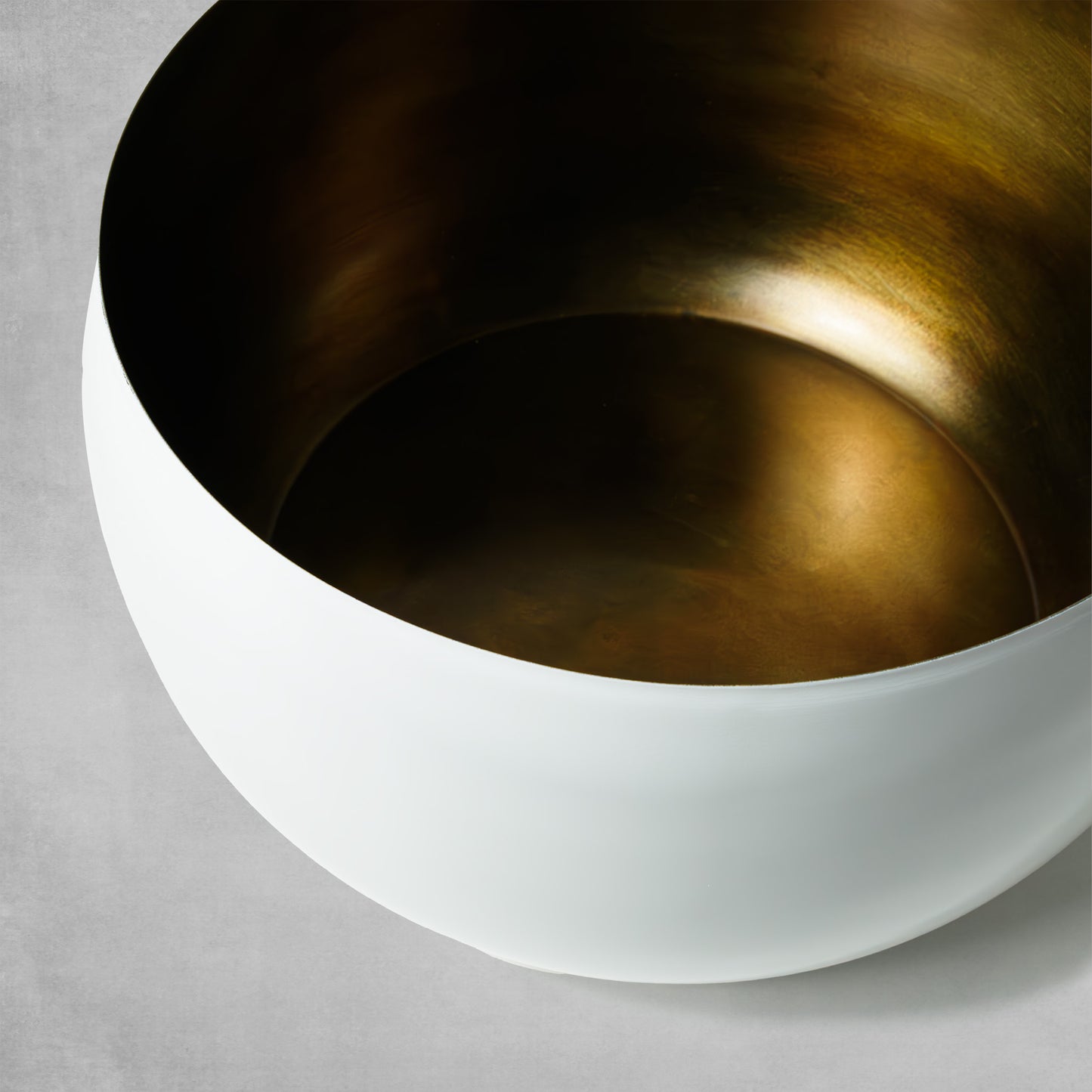 Decorative large white bowl with antique brass finish on gray background.
