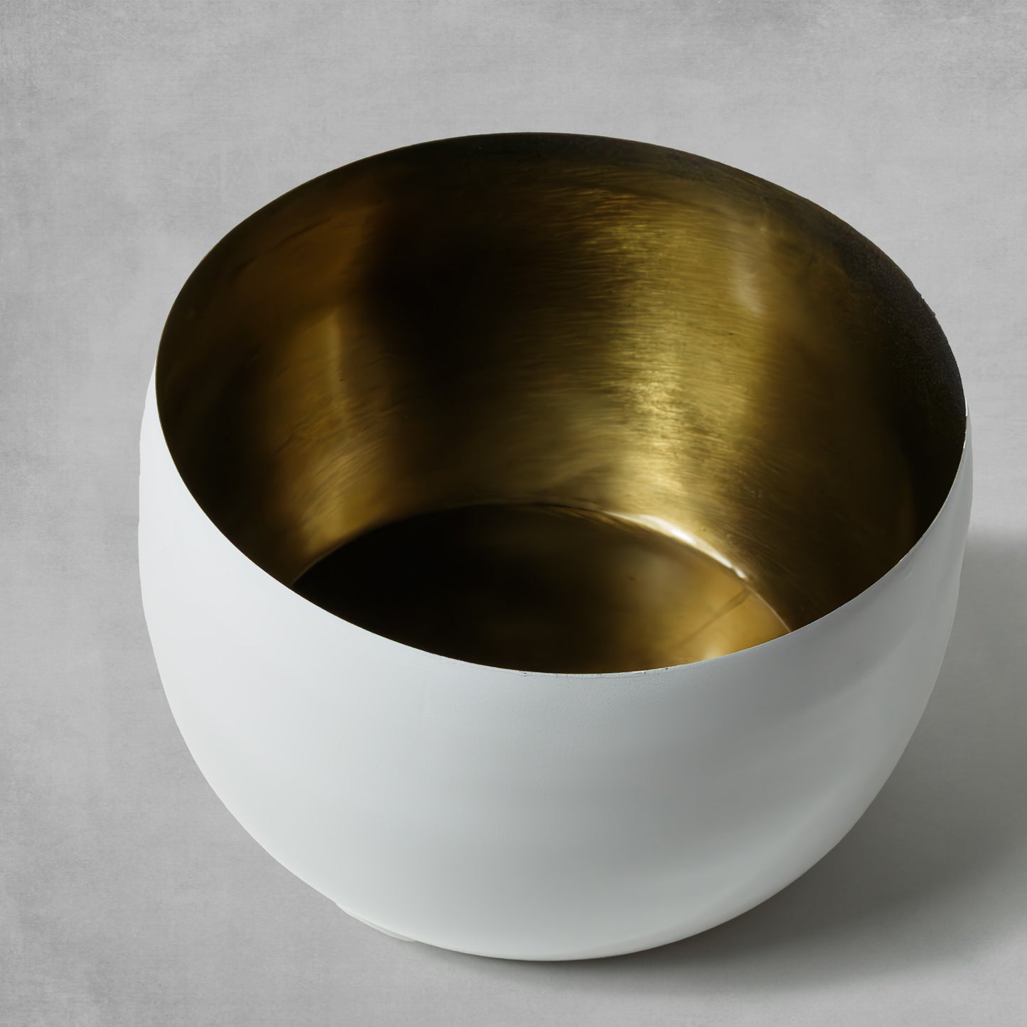 Decorative medium white bowl with antique brass finish on gray background.