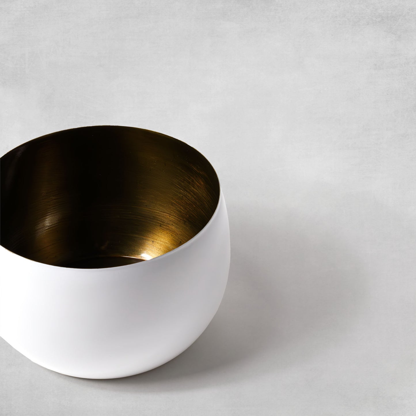 Decorative small white bowl with antique brass finish on gray background.
