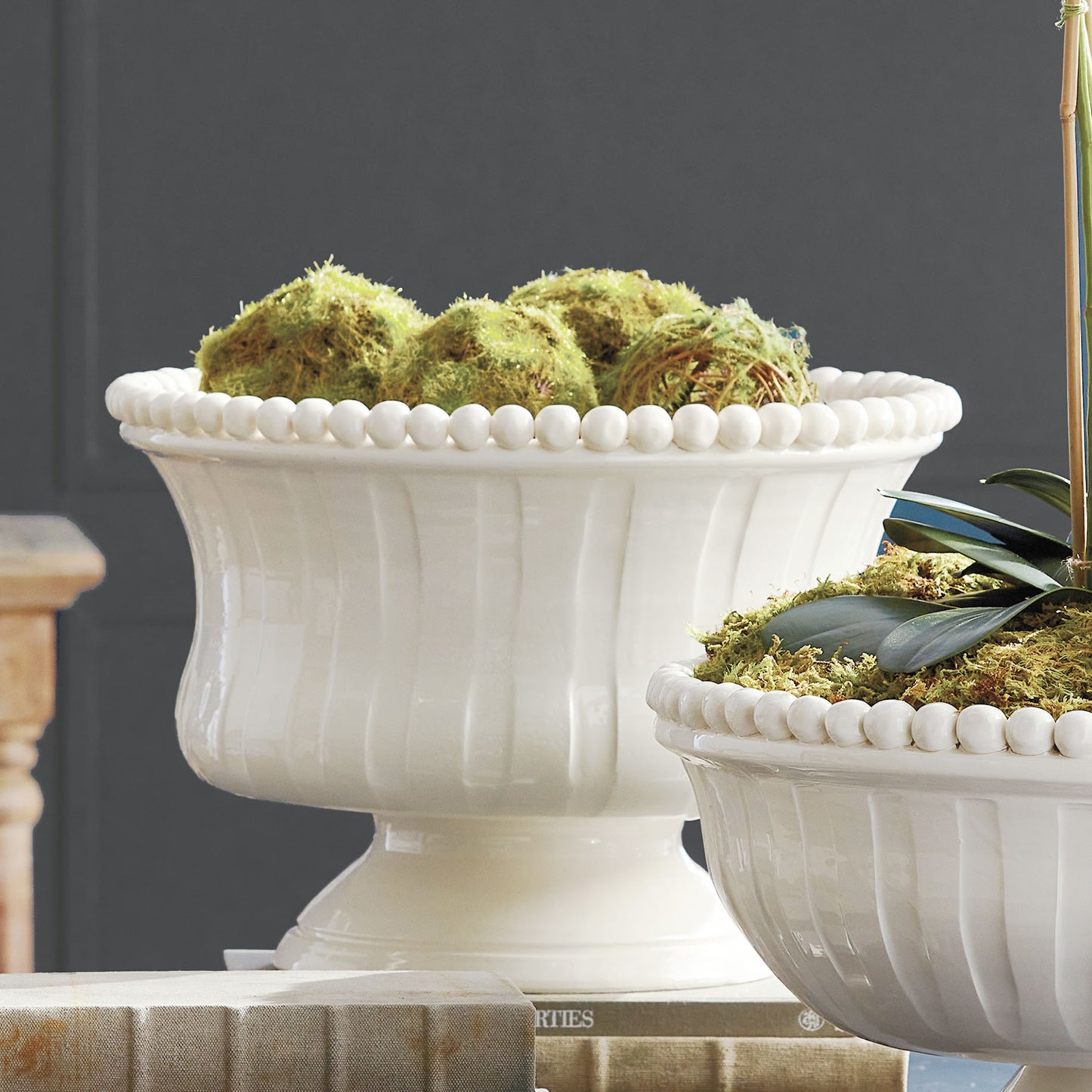 Decorative white ceramic footed bowl filled with moss balls stylized on table.