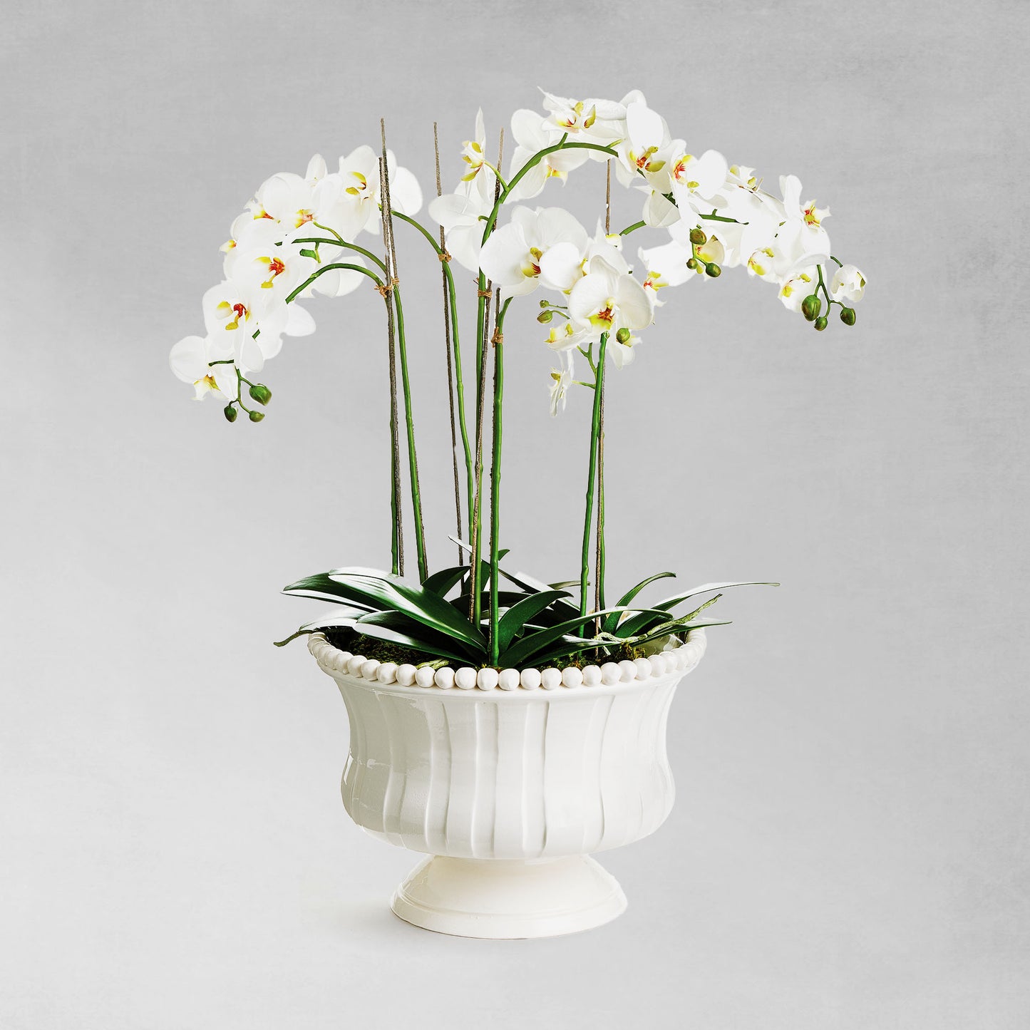 Decorative white ceramic footed bowl stylized with faux orchid drop-in, with gray background.