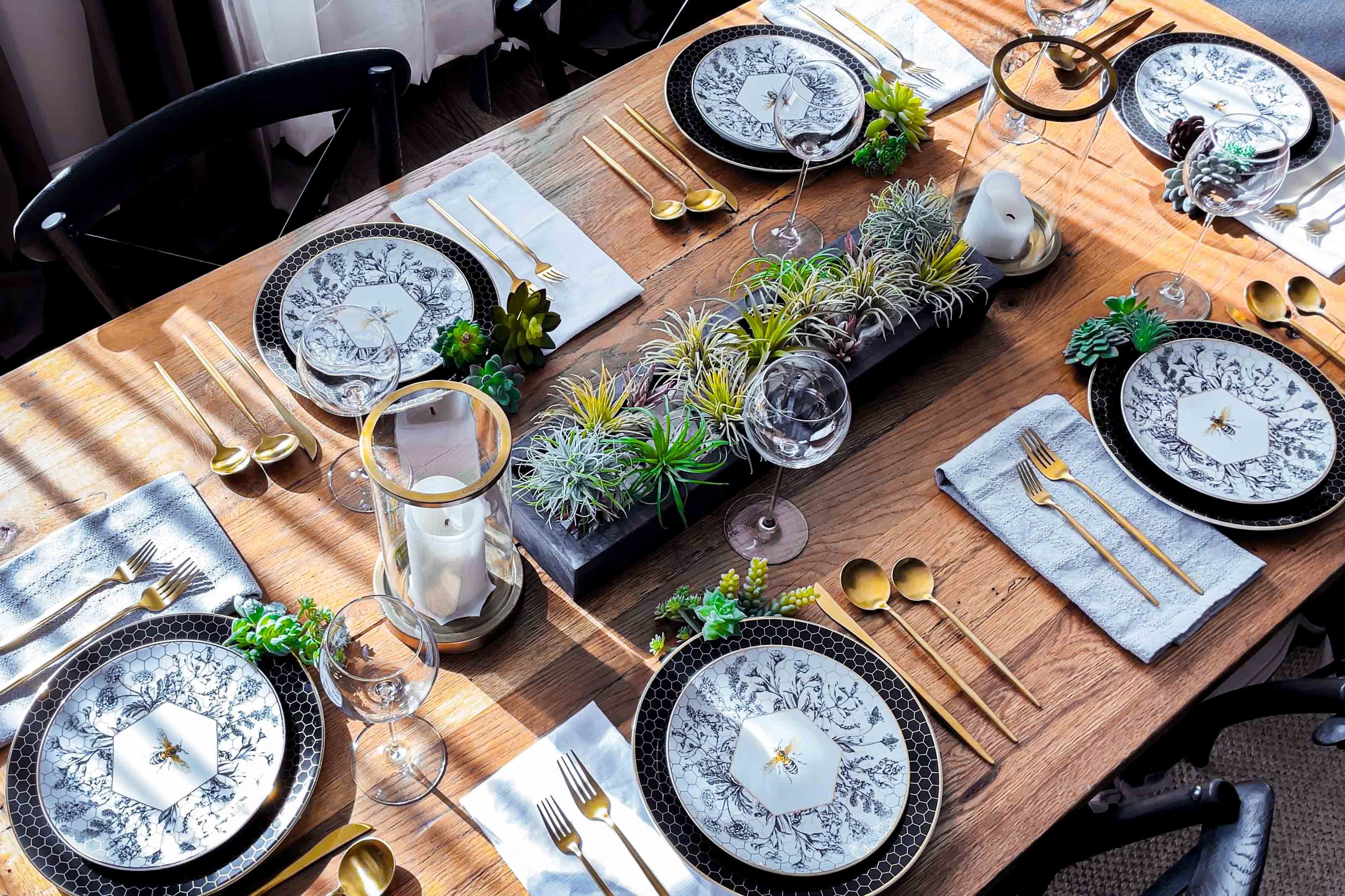 Farmhouse table set with gold flatware, honeybee dinnerware, candles, and succulents.