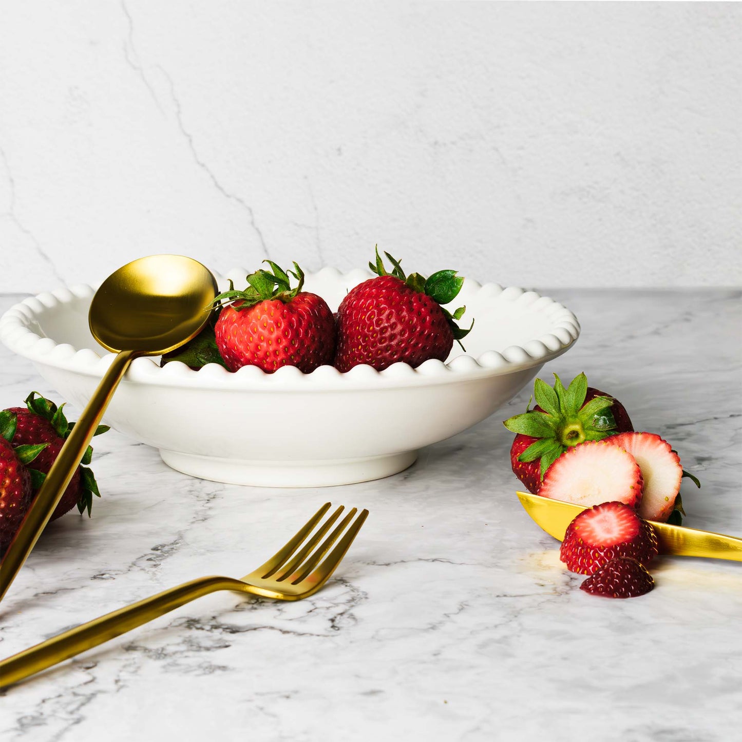 Flatware set in brushed gold, with strawberries in bowl, on marble table.
