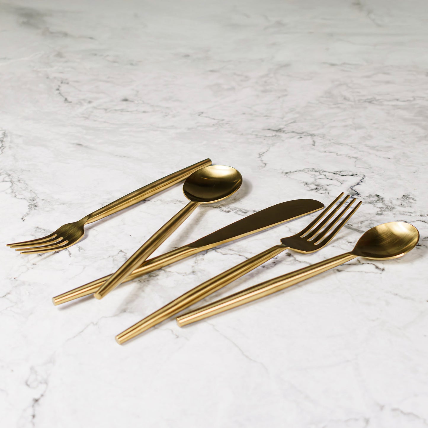 Matte gold flatware set stylized on marble tabletop.