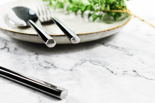 Flatware set with geometric mirrored finish on stoneware plate with greenery.