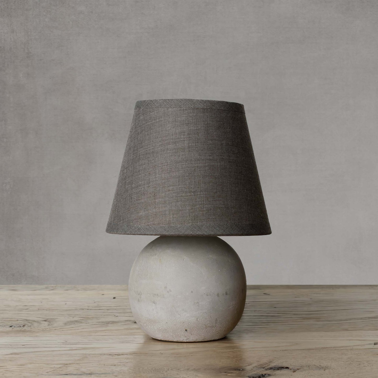 Gray concrete mini lamp with dark gray shade on wooden surface with light gray background.