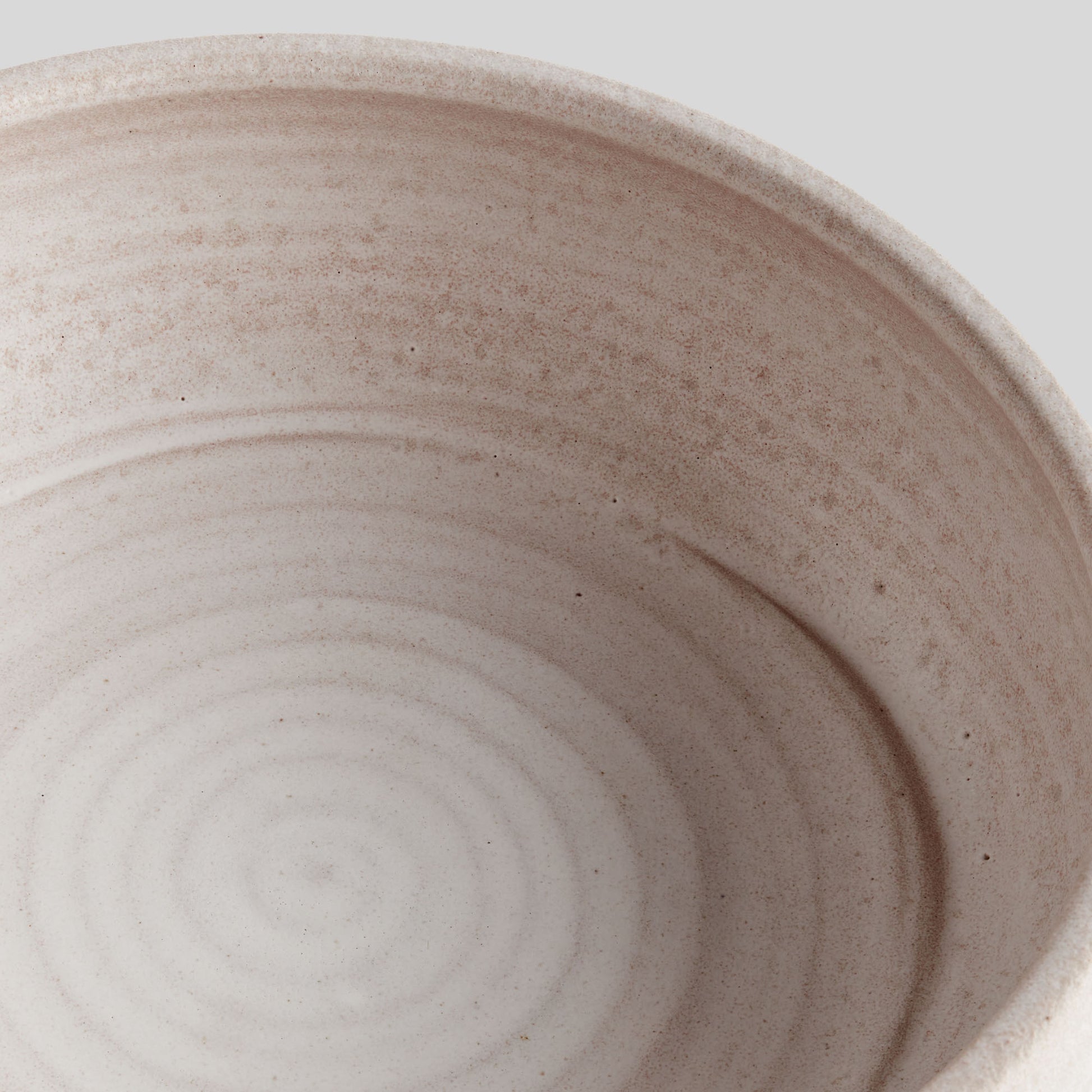 Hand-thrown white ceramic decorative bowl, closeup view, with gray background.