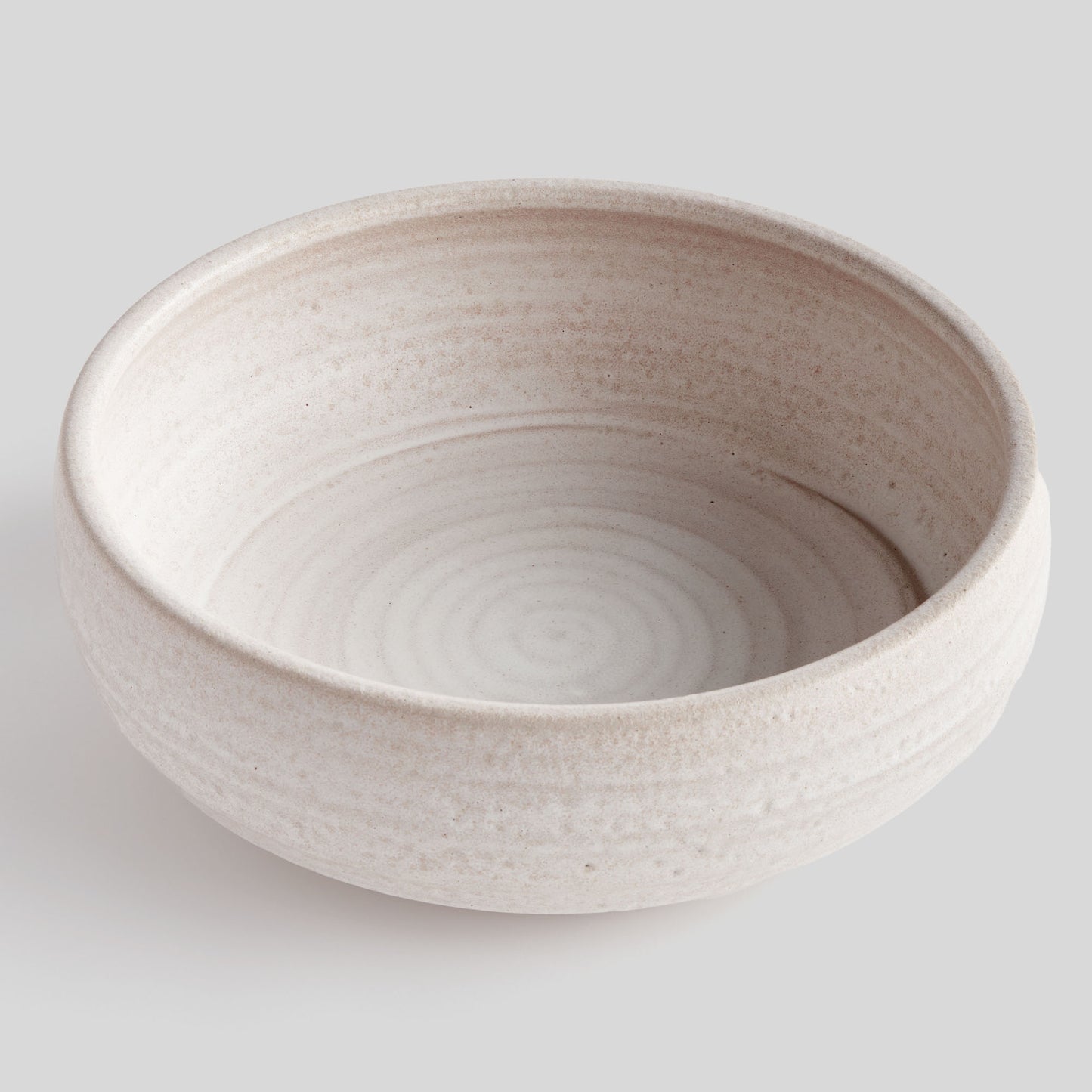 Hand-thrown white ceramic decorative bowl, top view, with gray background.