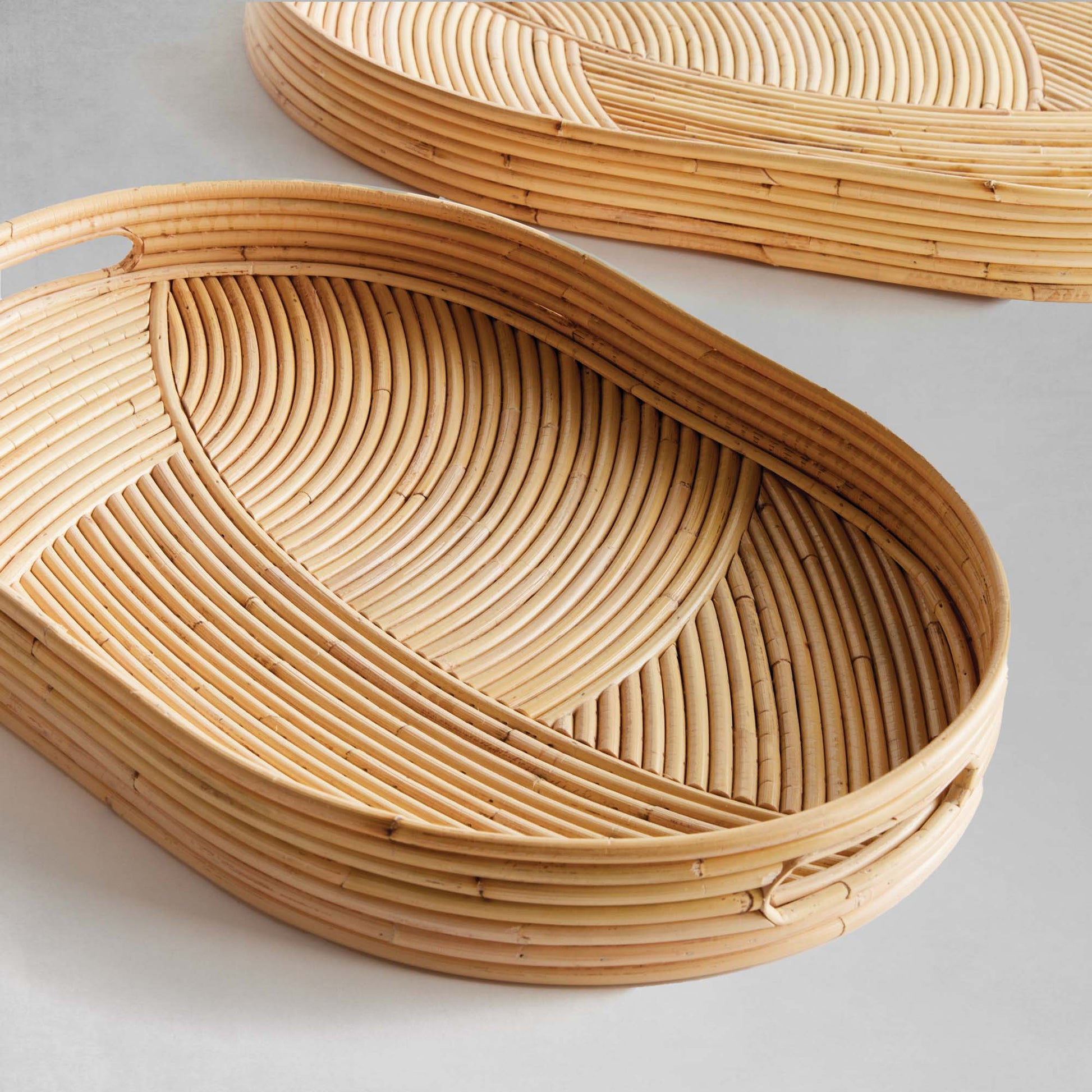 Handwoven oval rattan serving trays, front view, on gray background.