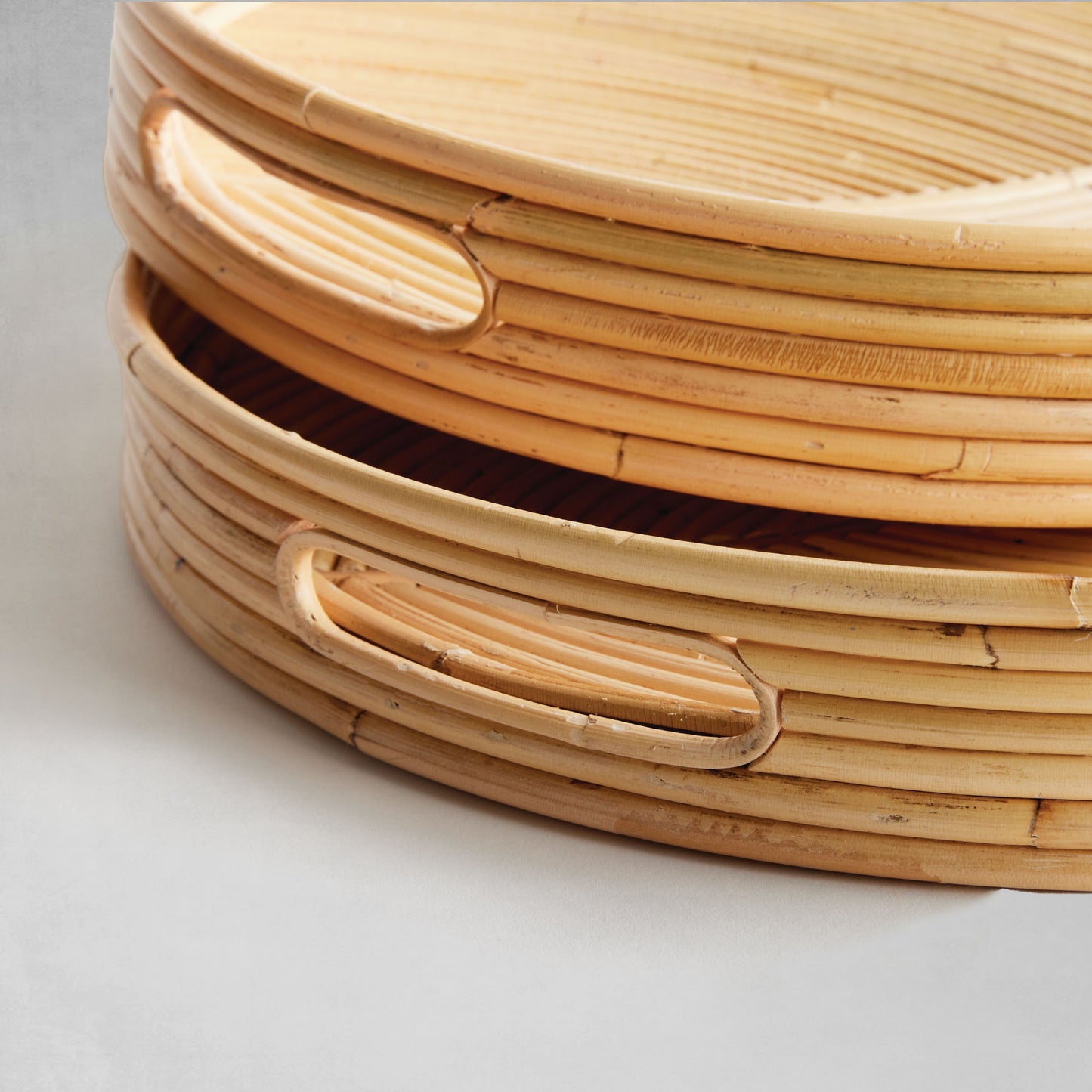 Handwoven oval rattan serving trays, closeup view, on gray background.