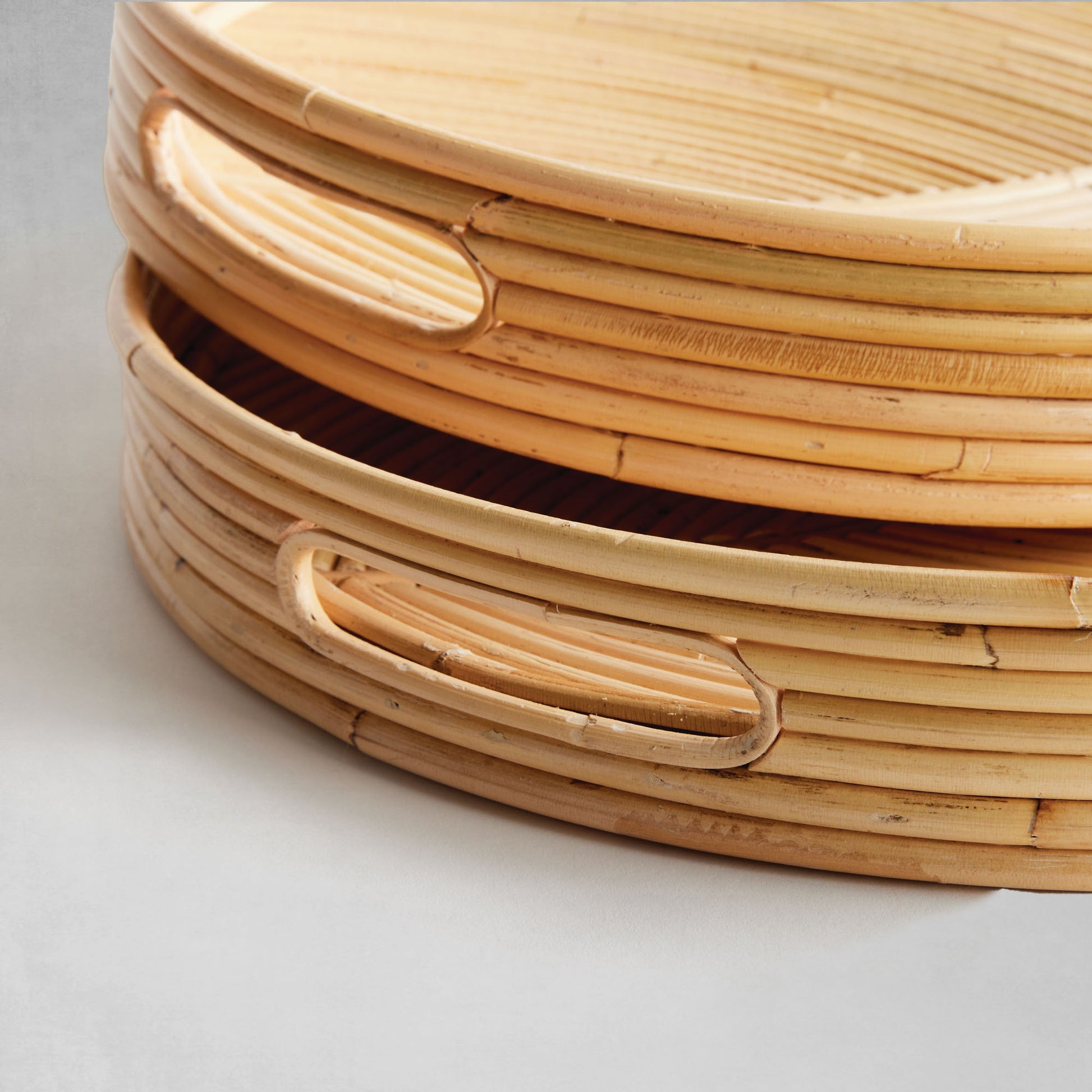 Handwoven oval rattan serving trays, closeup view, on gray background.