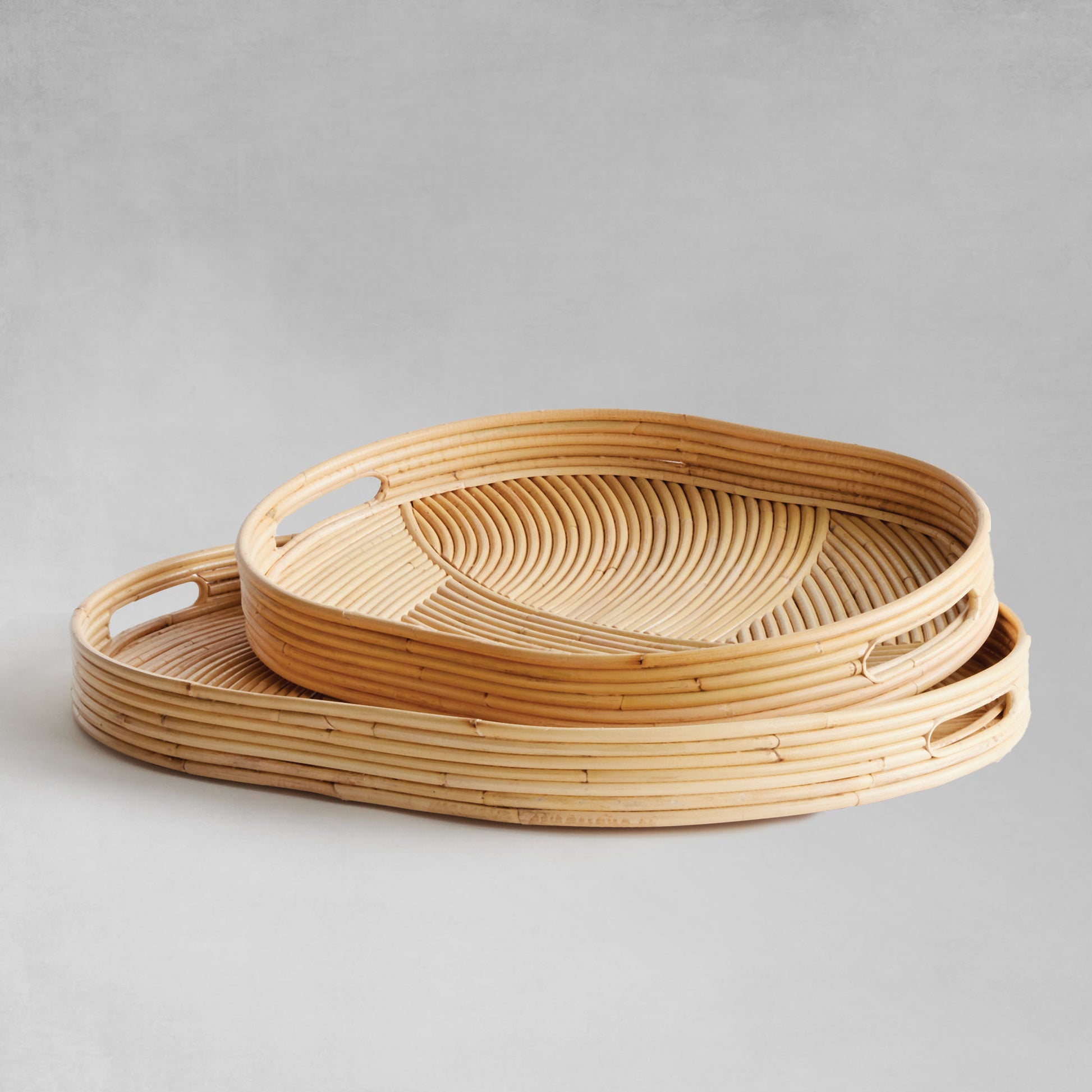 Handwoven oval rattan serving trays stacked on gray background.