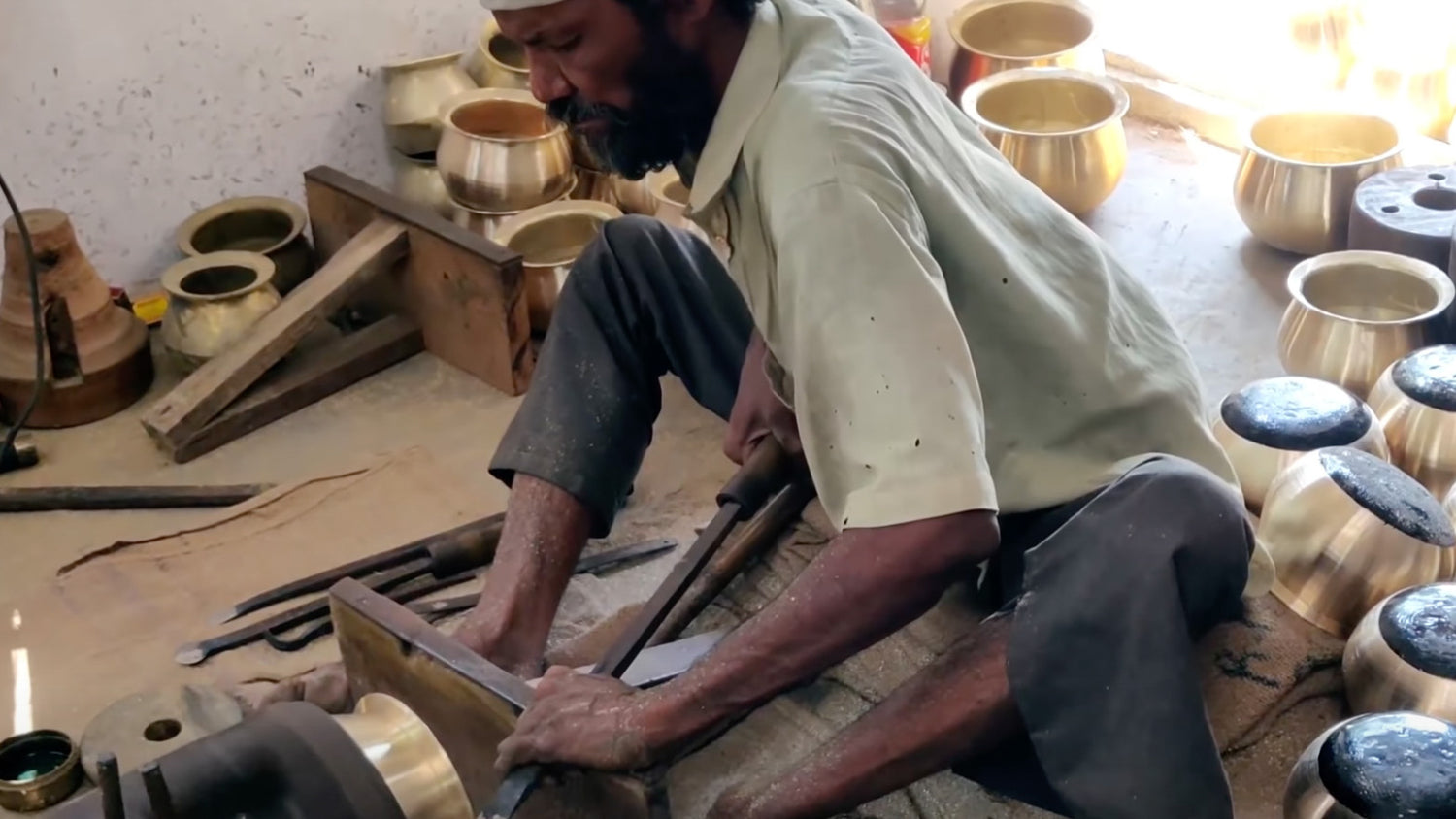 Indian metalware artisan scraping metal bowls.