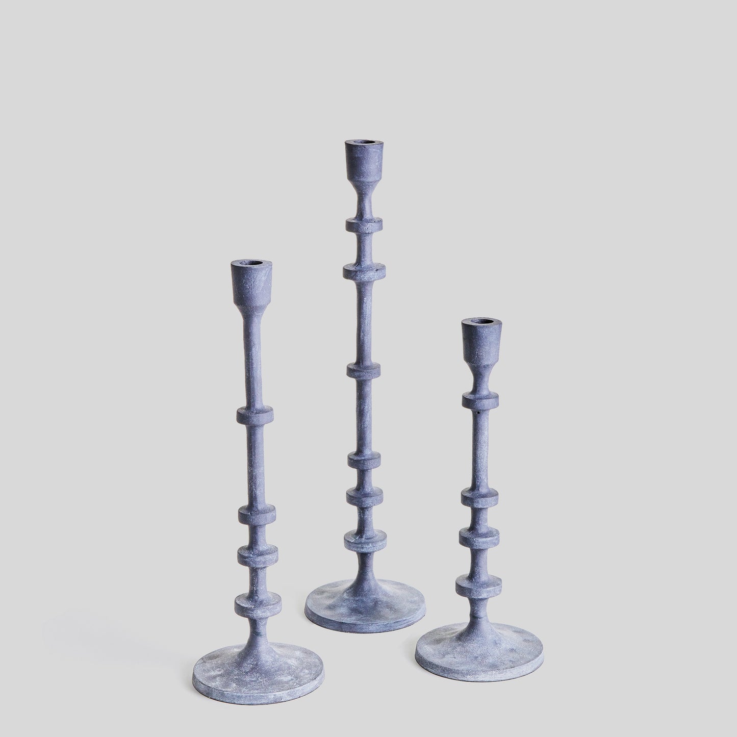 Set of three minimalist taper candleholders in aged zinc finish with gray background.