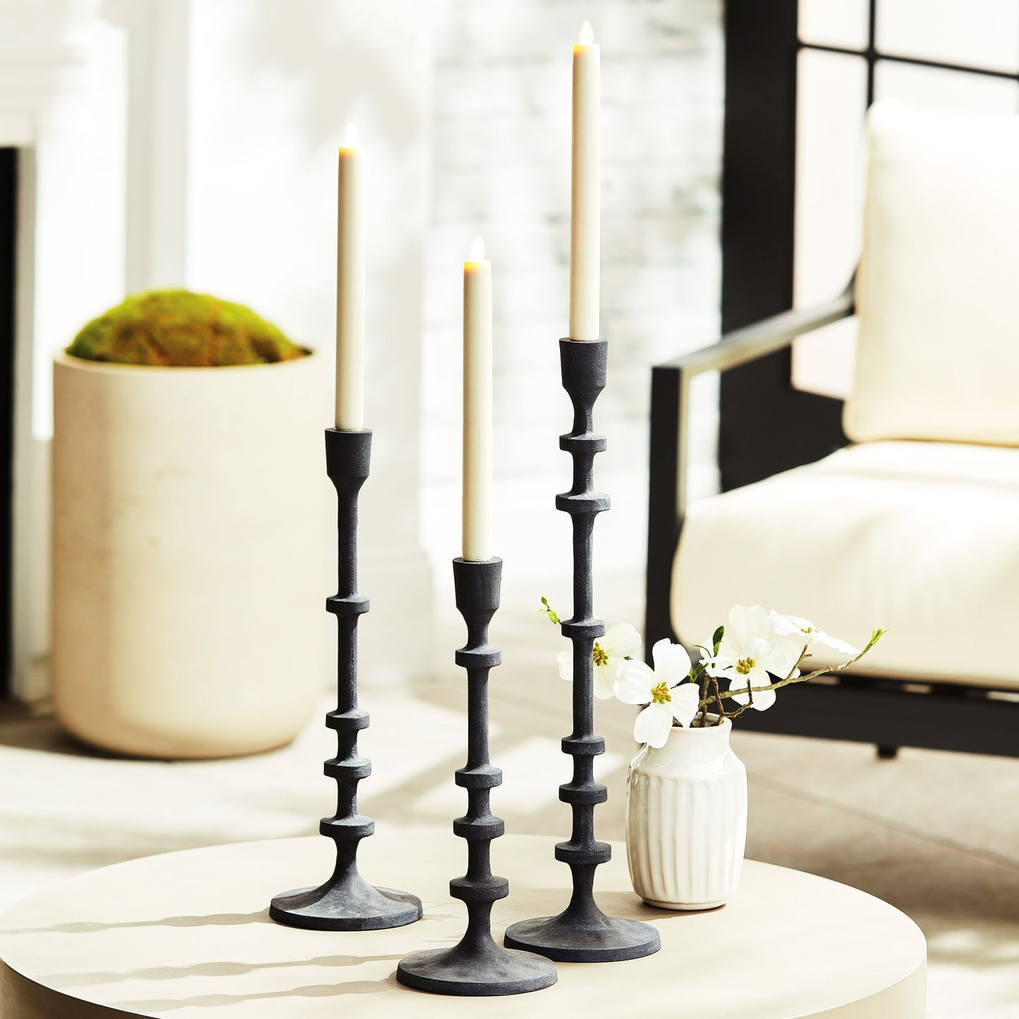 Set of three minimalist taper candleholders with bronze finish, stylized on round table in living room.