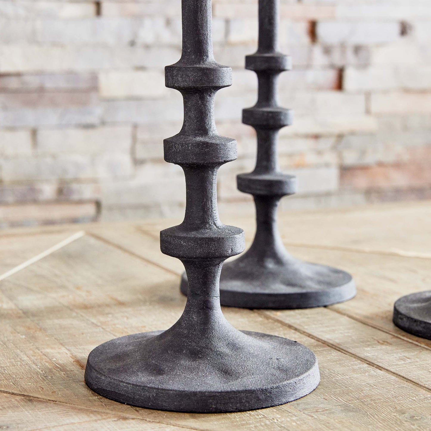 Set of three minimalist taper candleholders in bronze, closeup view, on wood table.