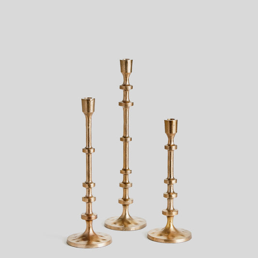 Set of three minimalist taper candleholders in gold with gray background.