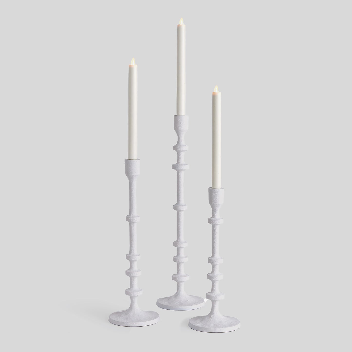 Set of three minimalist taper candleholders in white with gray background.