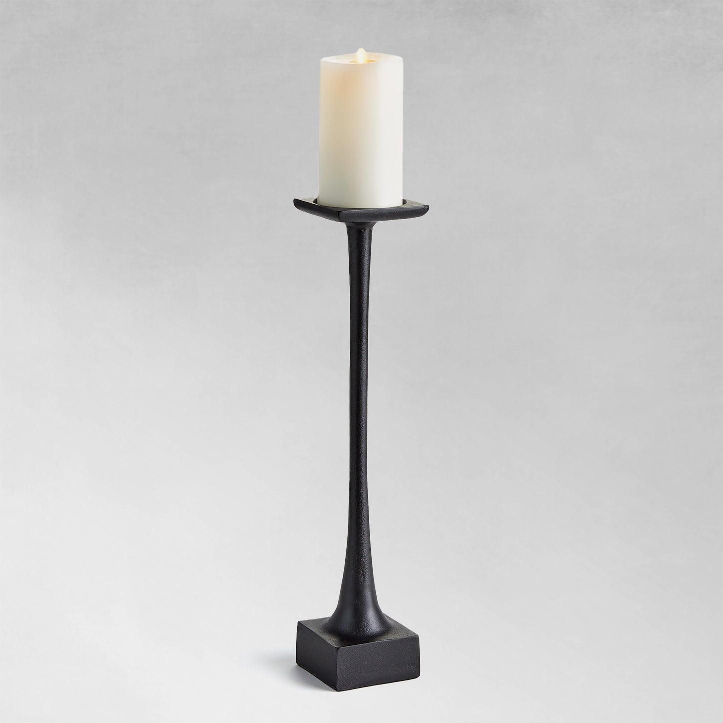 Large modern pillar candleholder with black finish and gray background.