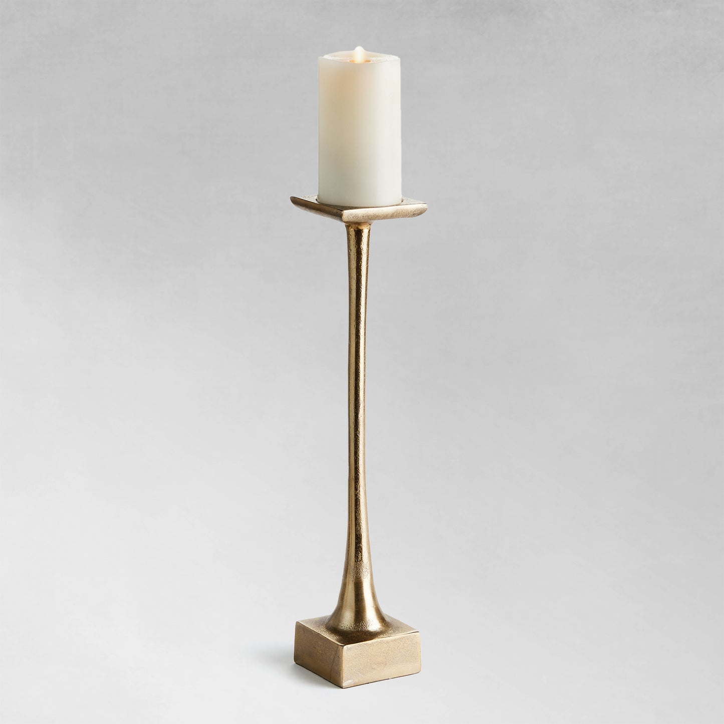 Large modern pillar candleholder with champagne finish and gray background.
