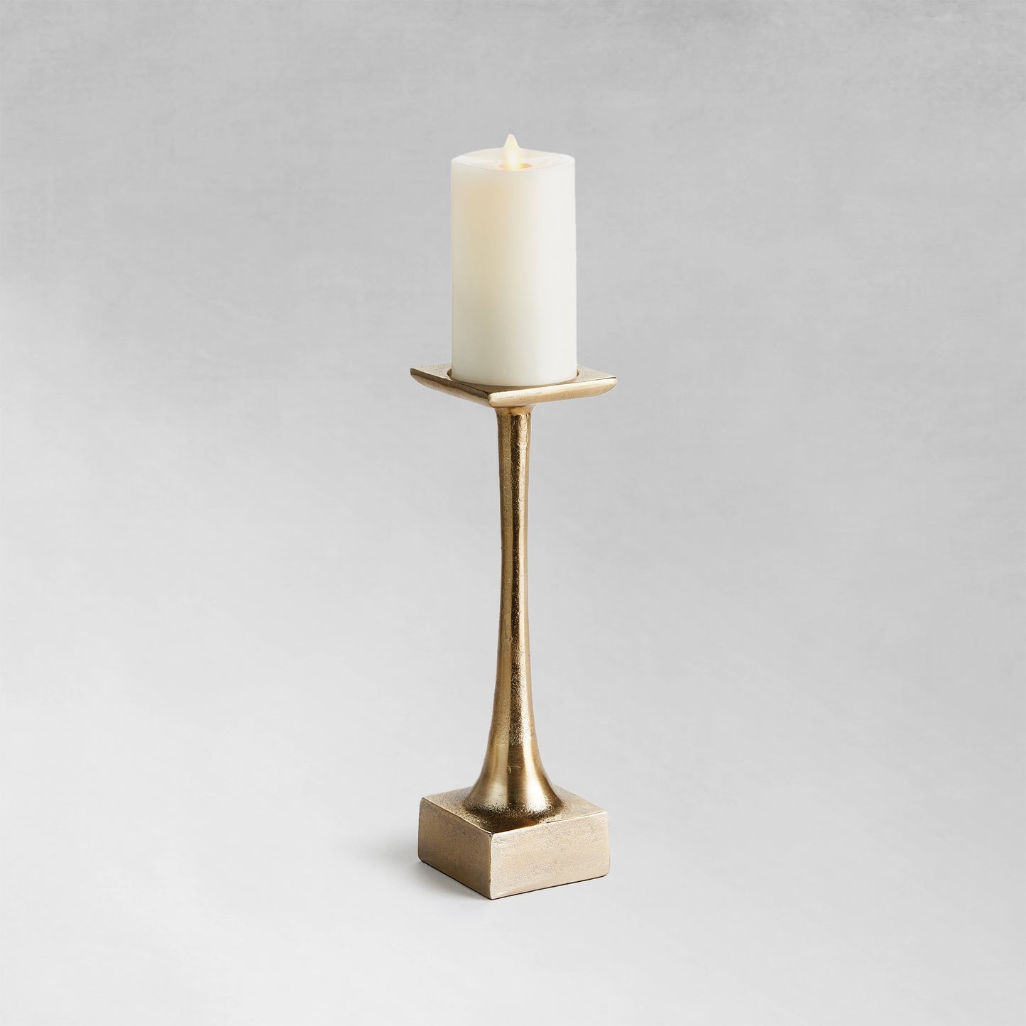 Small modern pillar candleholder with champagne finish and gray background.