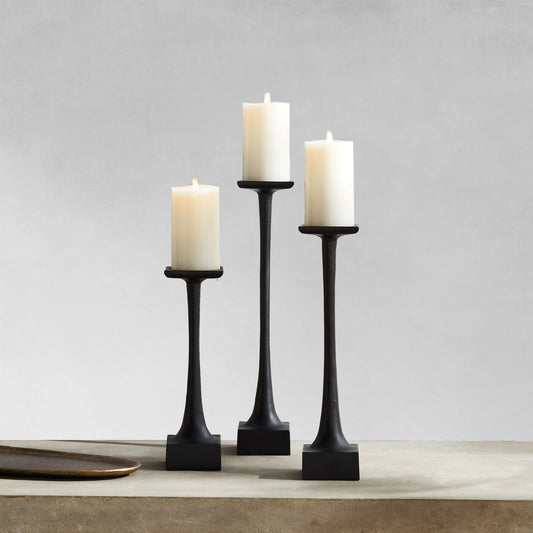 Modern pillar candleholders, small, medium and large, with black finish on table with gray background.