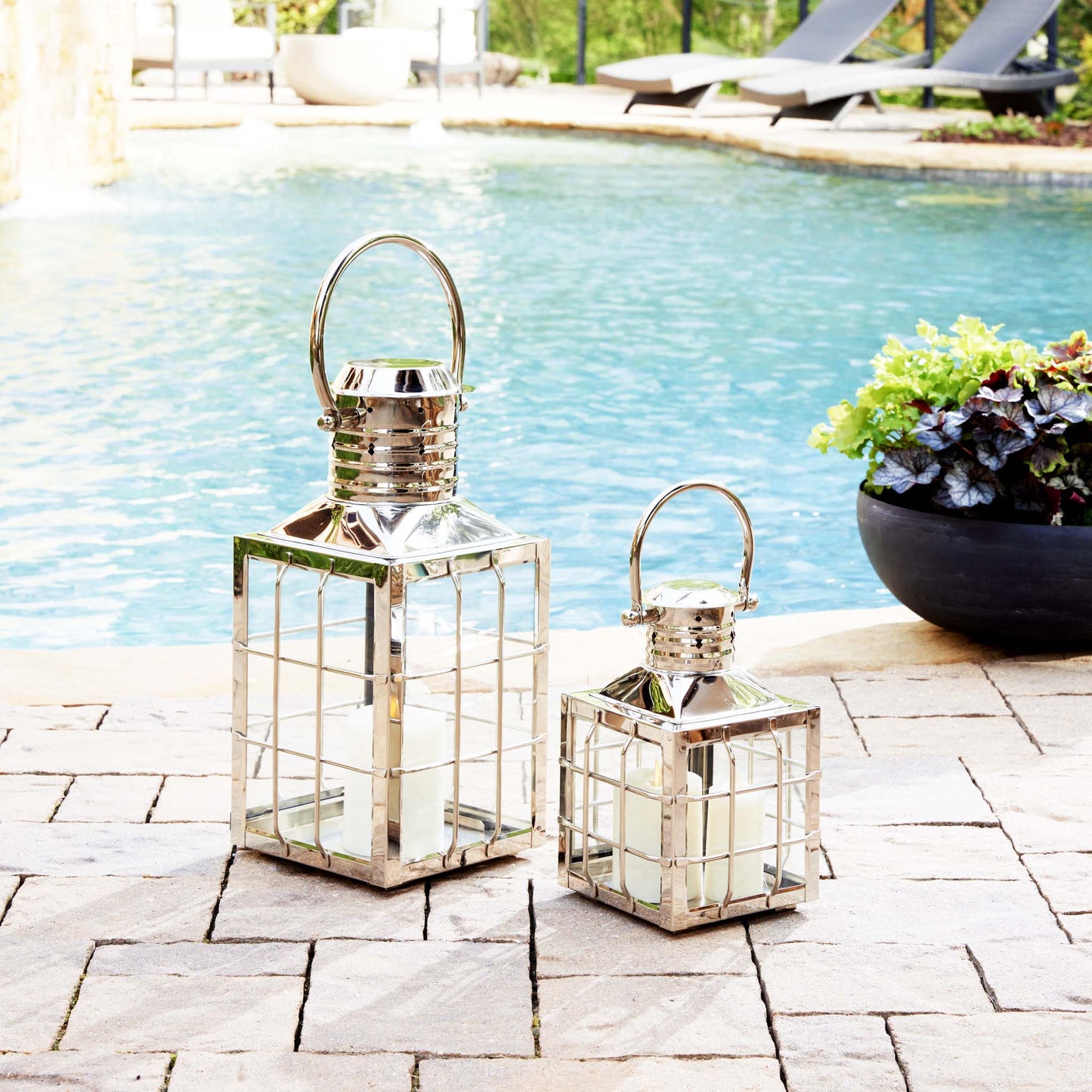 Nautical polished metal outdoor lanterns stylized next to pool with blue water.