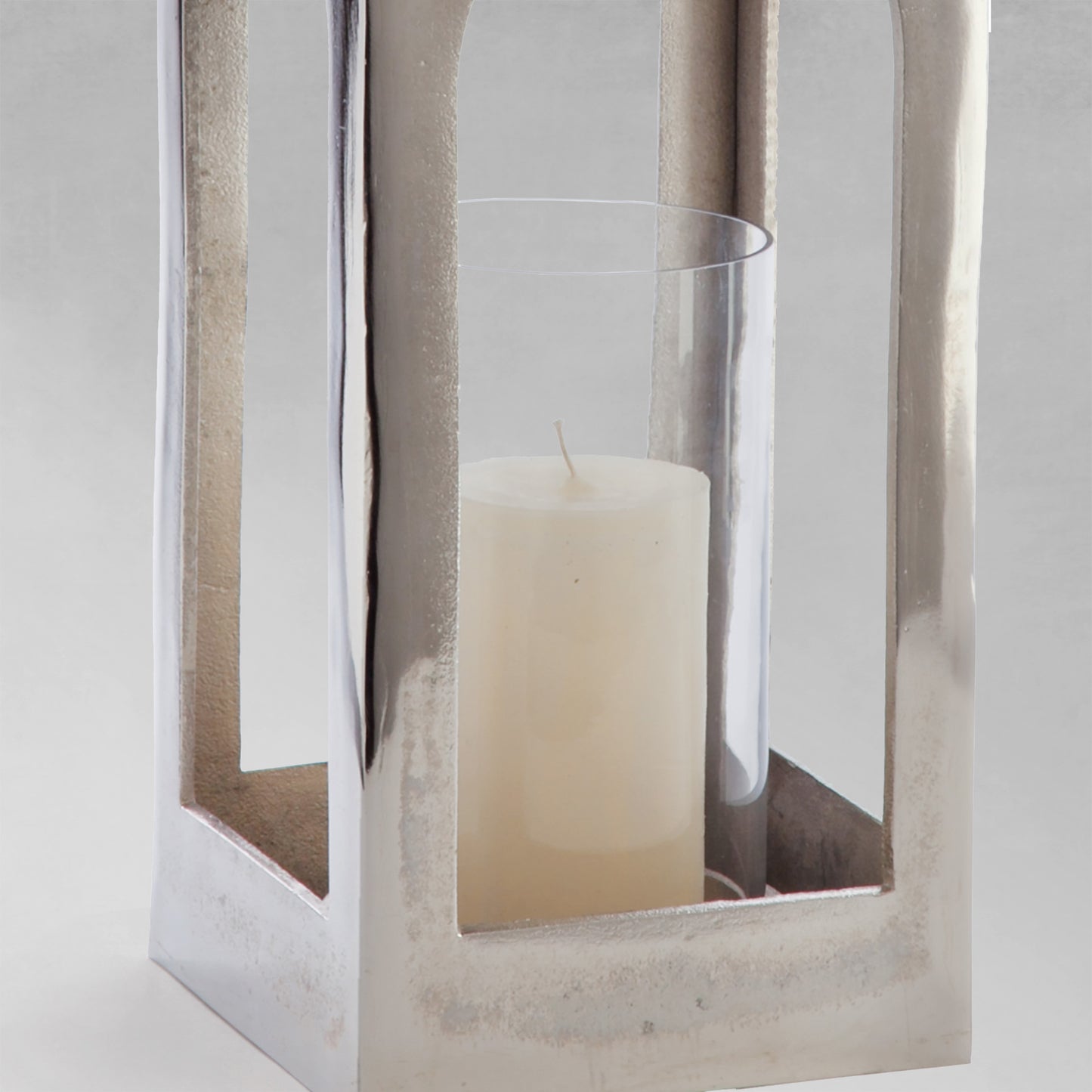 Polished metal lantern, closeup view of candle holder, with gray background.