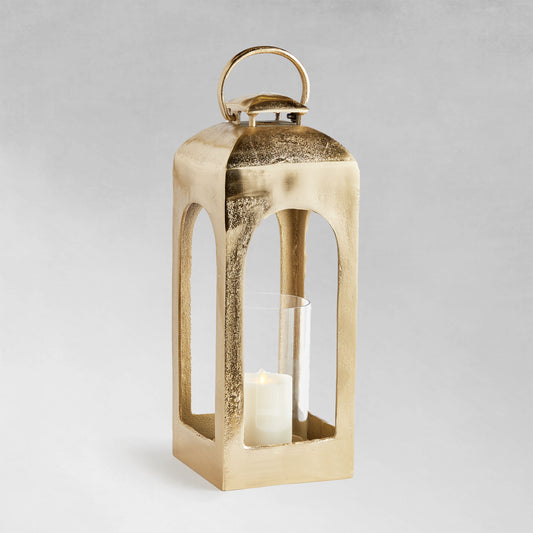 Small polished metal lantern with champagne finish on gray background.